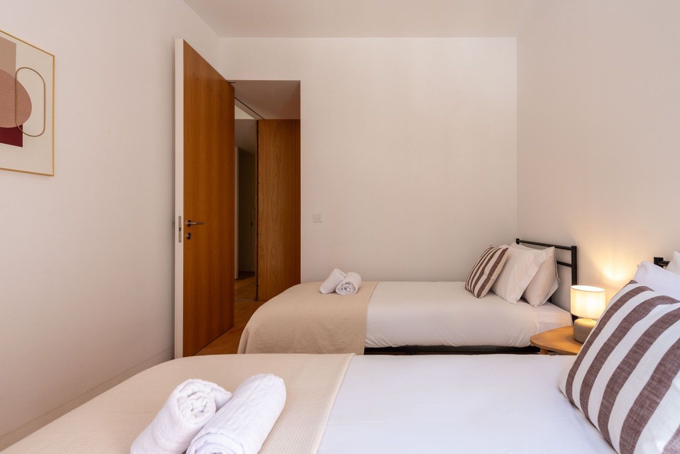 Ein Hotelzimmer mit zwei Betten, einer Holztür, einem Nachttisch mit Lampe und einem Wandbild.