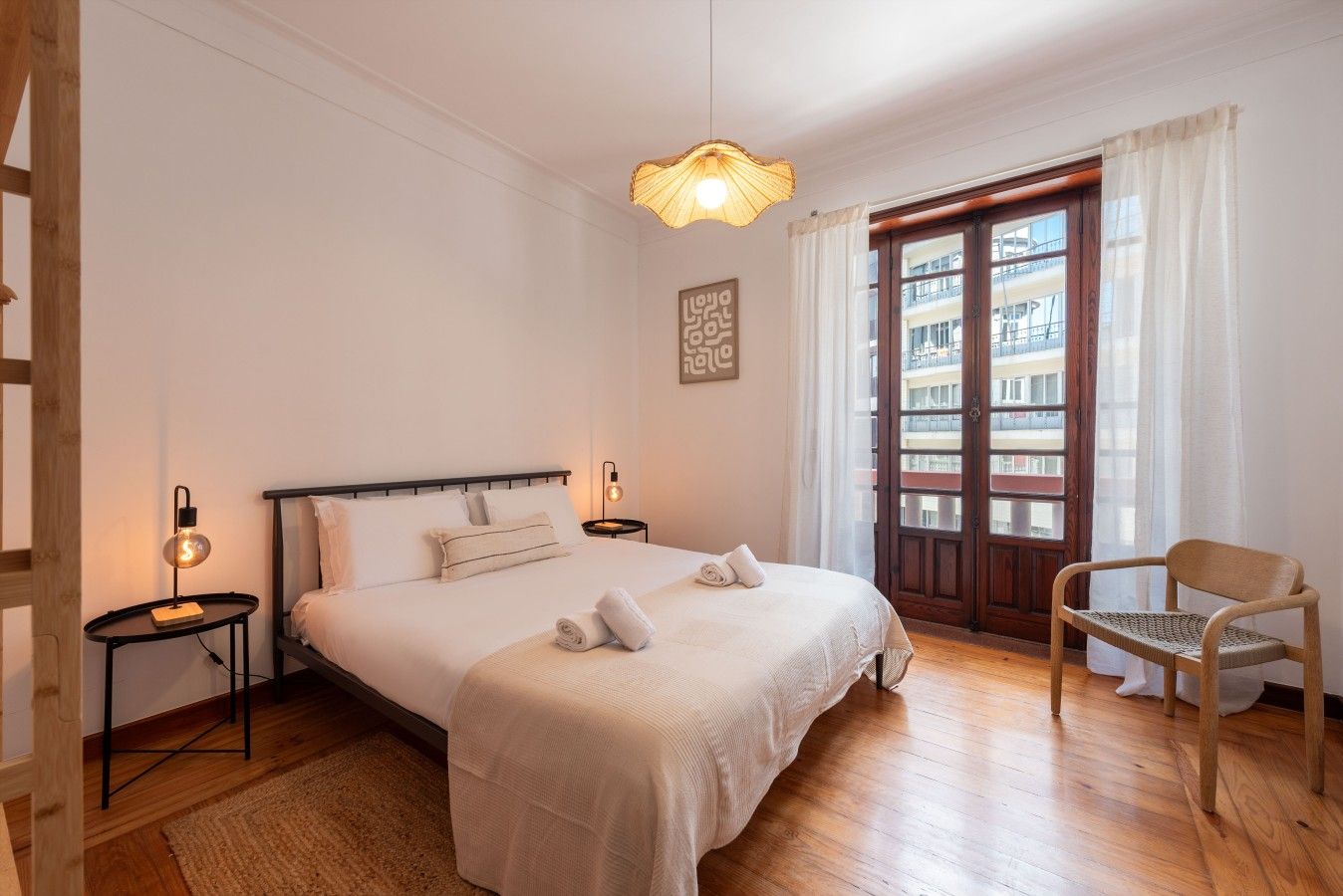 A hotel room with a bed, bedside tables, a chair, a window with curtains, and a view of buildings.
