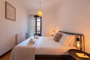 A hotel room with a bed, a bedside lamp, a wall-mounted light, a window with curtains, and a radiator. - Garça Real - Porto Group Apartment by Lisbeyond (Porto)