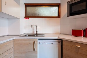 A compact kitchen with a dishwasher, a sink, and a red toaster on the countertop. - Garça Real - Porto Group Apartment by Lisbeyond (Porto)