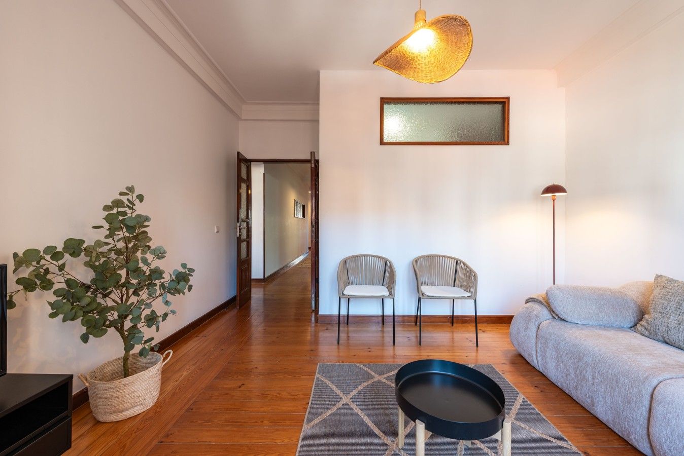 A living room with a sofa, two chairs, a floor lamp, a potted plant, and a framed picture on the wall.