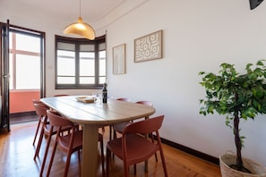 Un coin repas avec une table en bois, des chaises rouges, un luminaire suspendu, une plante en pot et des œuvres d’art accrochées au mur.