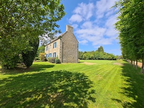 A stone building with blue shutters, surrounded by a well-maintained lawn and trees. - Charming Breton house (Ploumilliau)