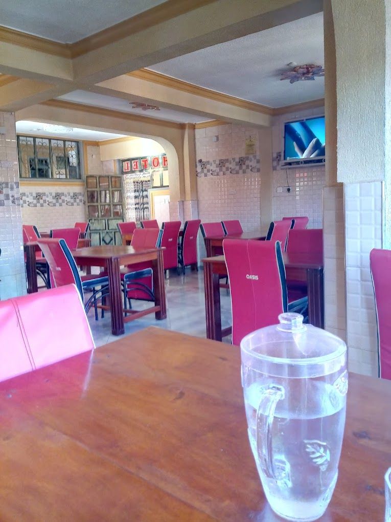 Un restaurant avec des chaises rouges et des tables en bois, un mur carrelé et un téléviseur fixé au mur.