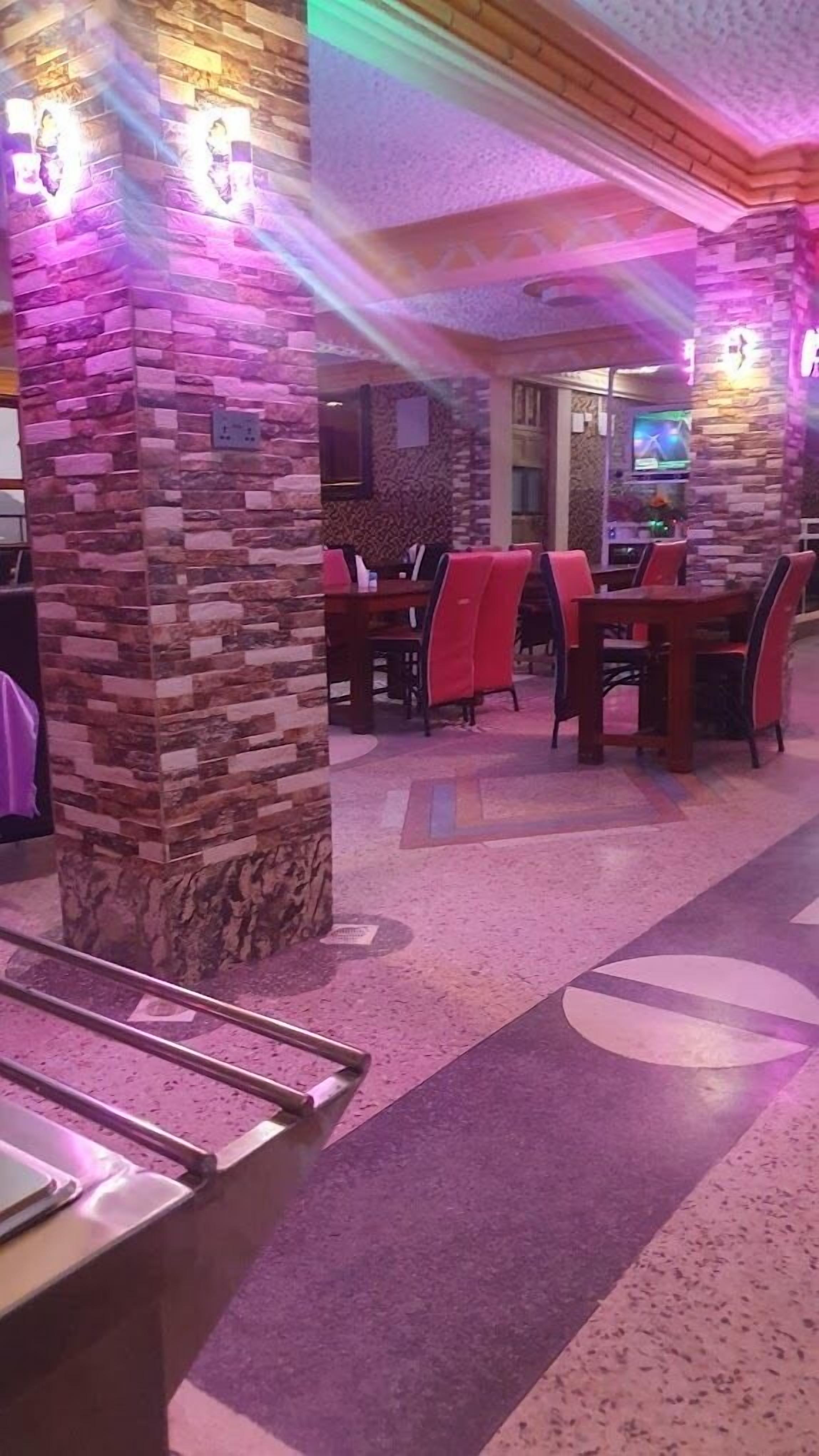 Een restaurant met stenen pilaren, rode stoelen en een betegelde vloer.
