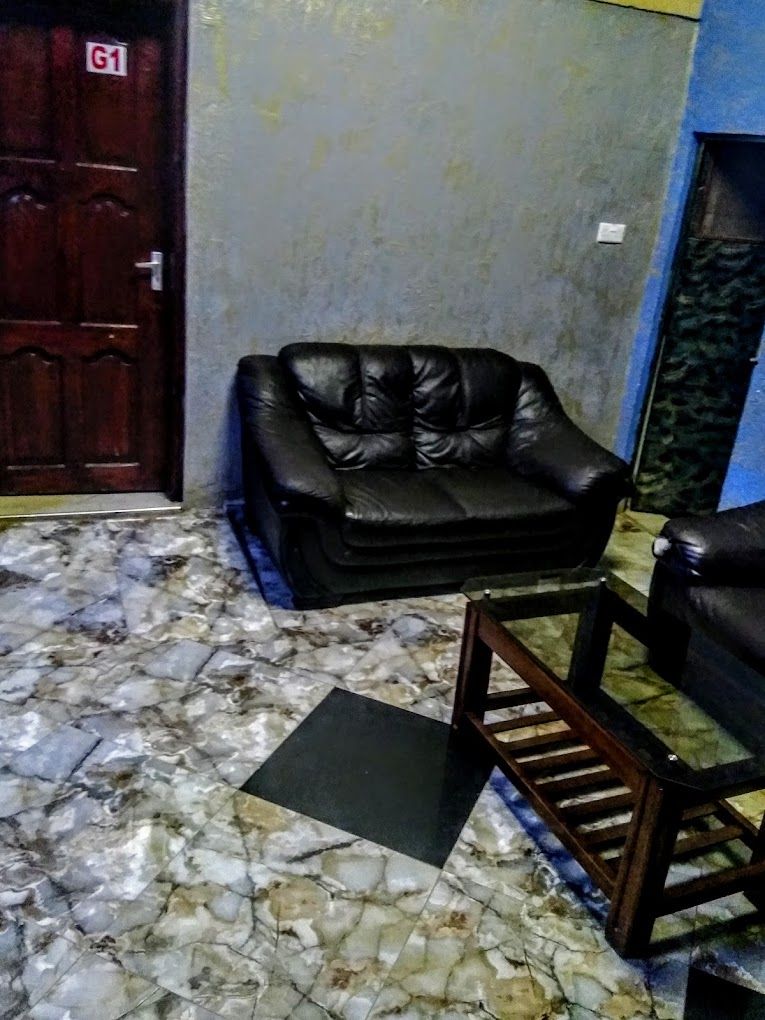 Una habitación con un sofá de cuero negro, una silla de madera y un suelo con diseño de mármol.