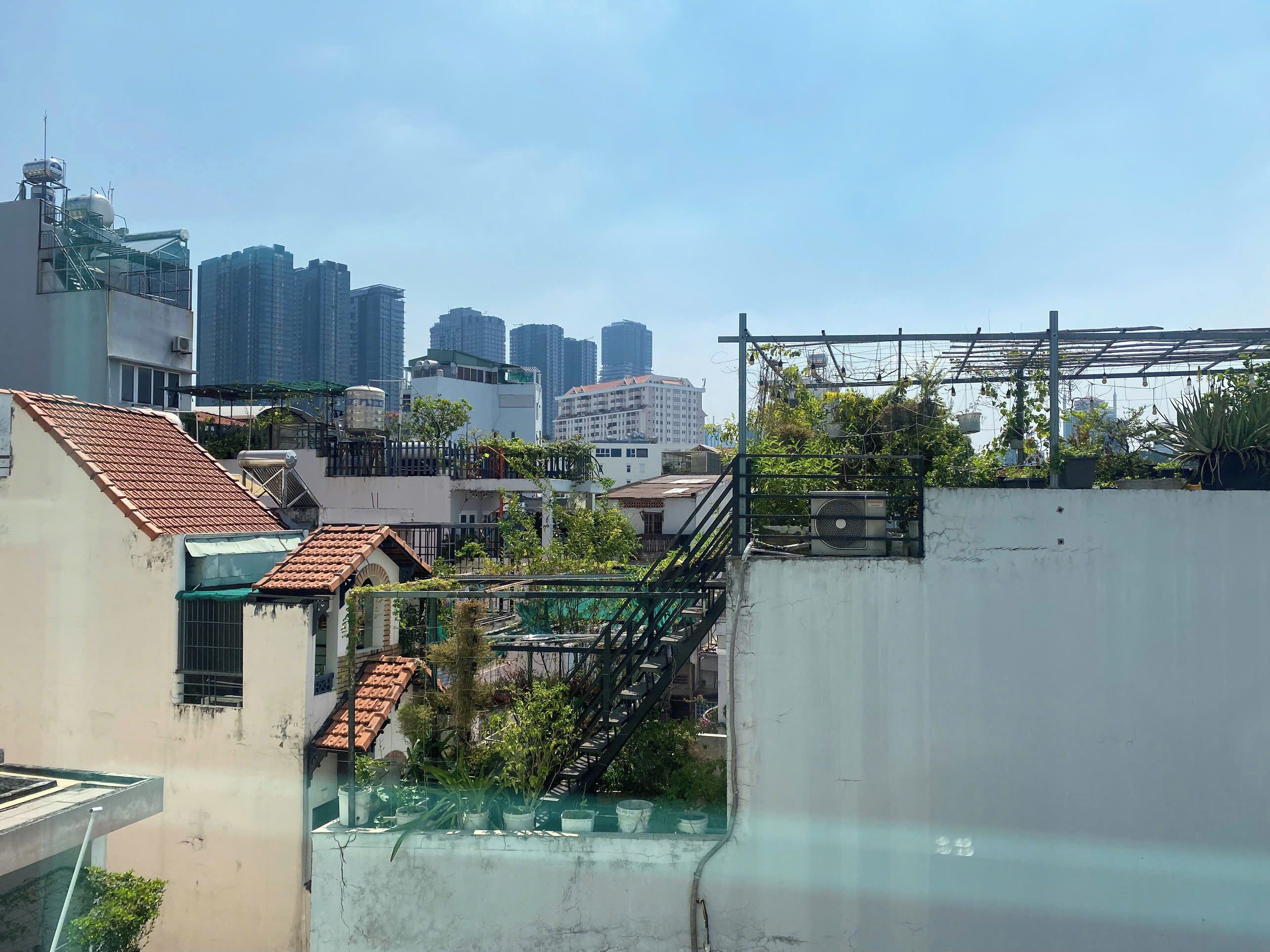 A rooftop terrace with a view of surrounding high-rise buildings, a staircase, and some greenery.