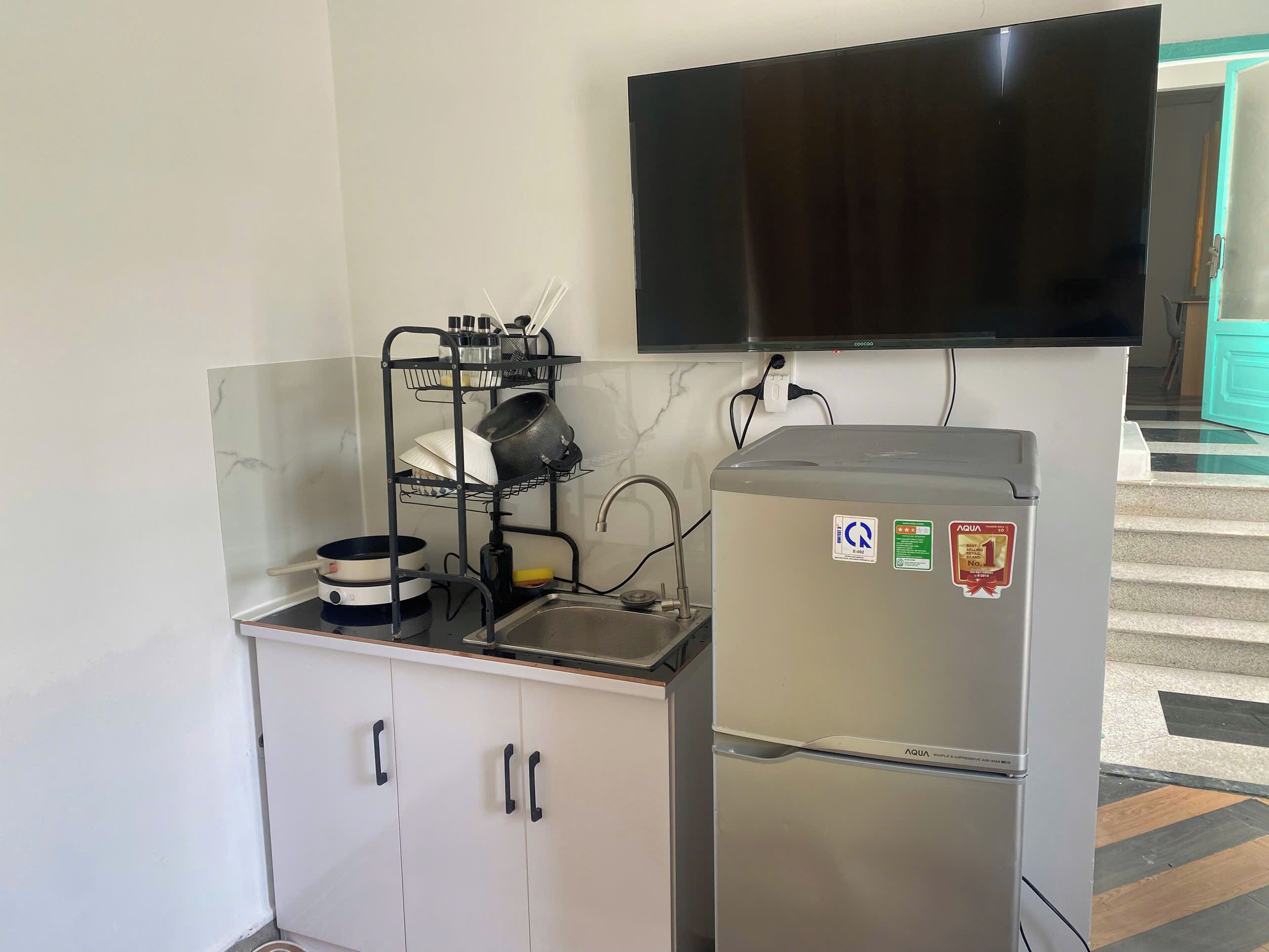 Una kitchenette con un refrigerador de acero inoxidable, un televisor negro montado arriba y un escurreplatos con ollas y sartenes.