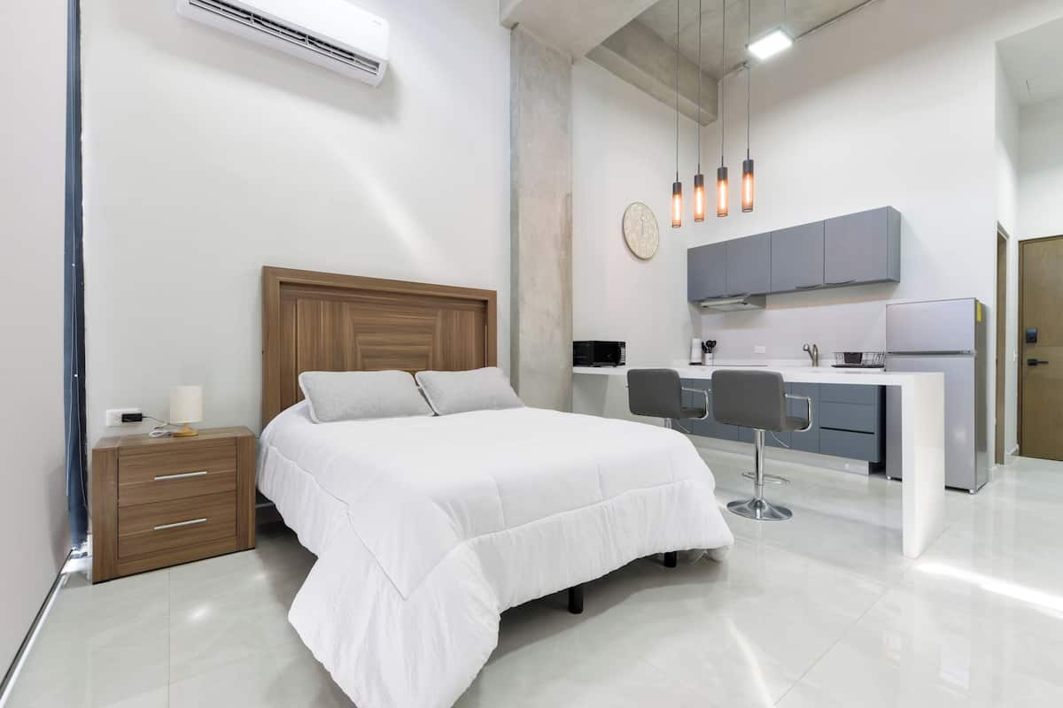 Un dormitorio moderno con cama, mesita de noche y una pequeña zona de escritorio con silla.