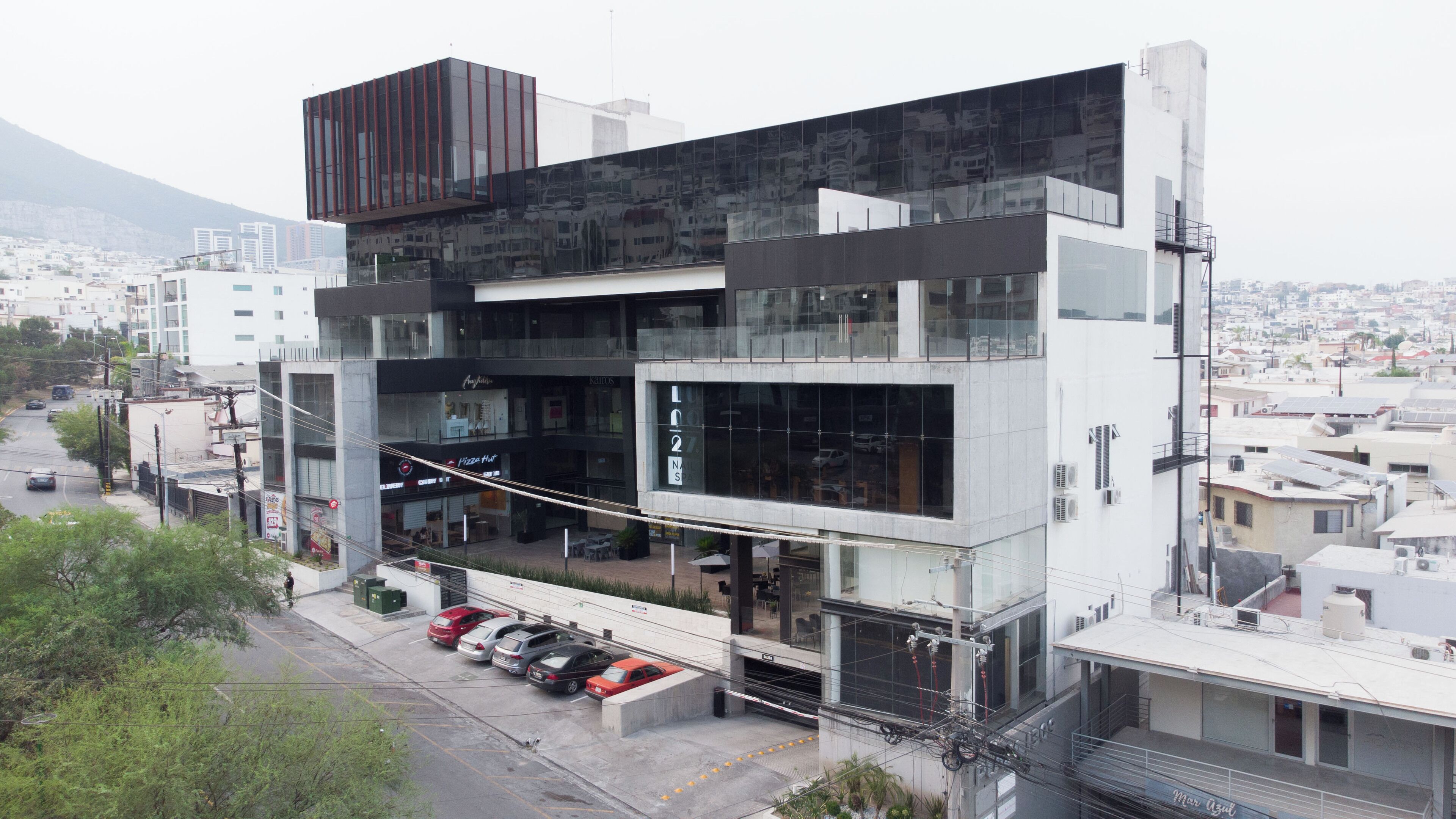 Um edifício moderno com fachada de vidro, vários andares e uma área de estacionamento com carros.