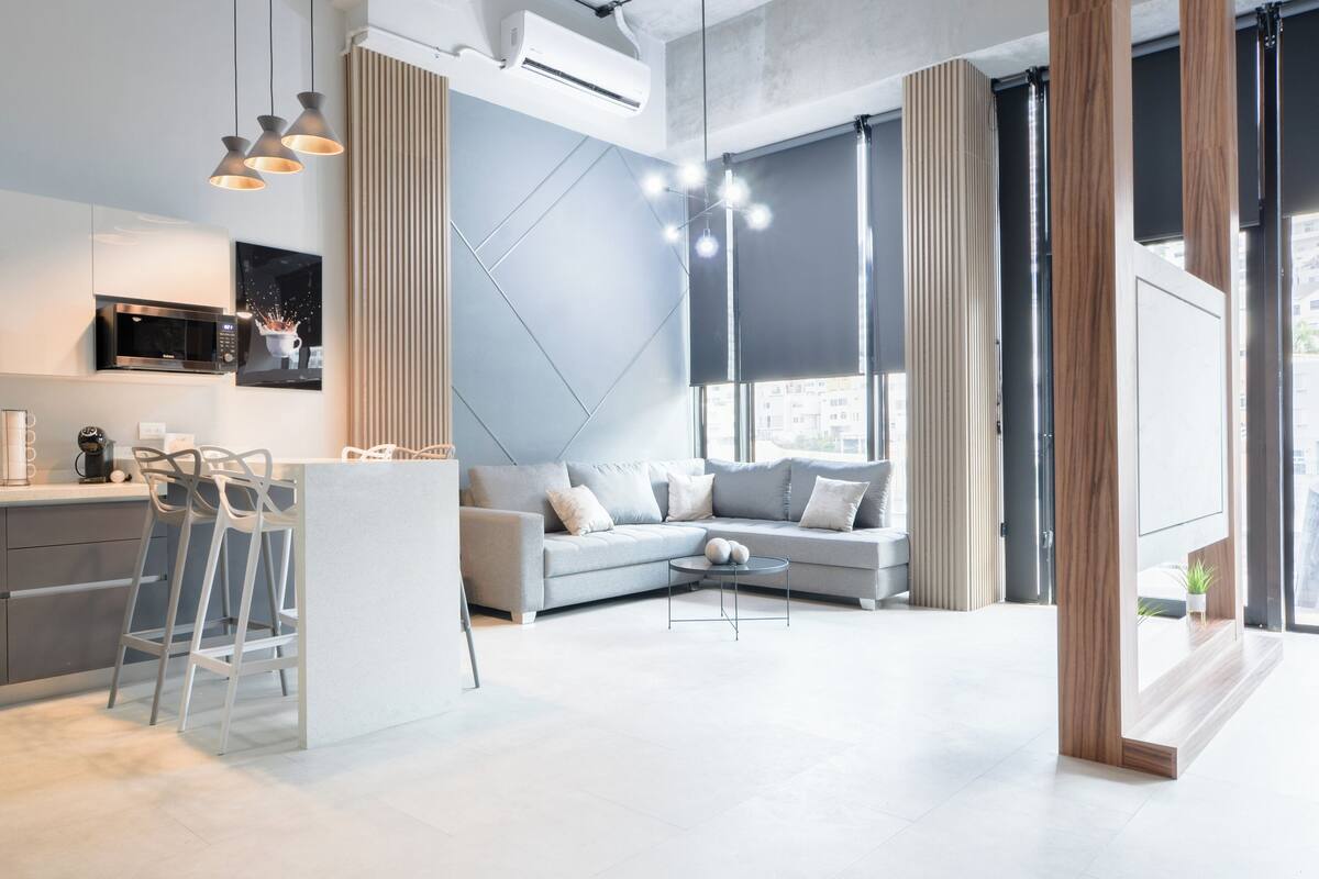 Un espacio habitable moderno con cocina, un sofá gris y una zona de comedor con taburetes de bar.