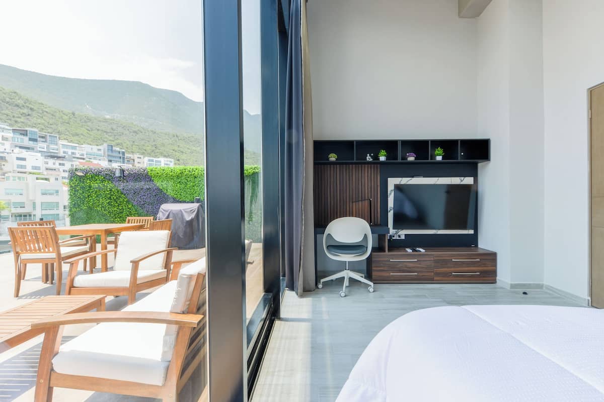 Una habitación de hotel moderna con balcón, televisión y zona de estar con sillas y una mesa.
