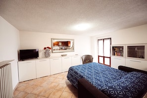 A bedroom with a bed, a TV, a chair, a dresser, and a window.