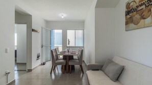A modern living room with a dining area, a sofa, and a large window. - Apt in Condo w/ Pool in Porto Seguro Tmr0104 (Porto Seguro)