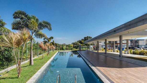 A swimming pool with a wooden deck, surrounded by palm trees and a covered walkway. - Apt in Condo w/ Pool in Porto Seguro Tmr0104 (Porto Seguro)