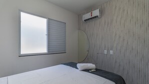 A hotel room with a bed, a window with blinds, an air conditioning unit, a mirror, and a towel on the bed. - Apt in Condo w/ Pool in Porto Seguro Tmr0104 (Porto Seguro)