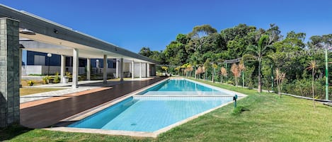 A modern house with a swimming pool, covered patio, and lush greenery.