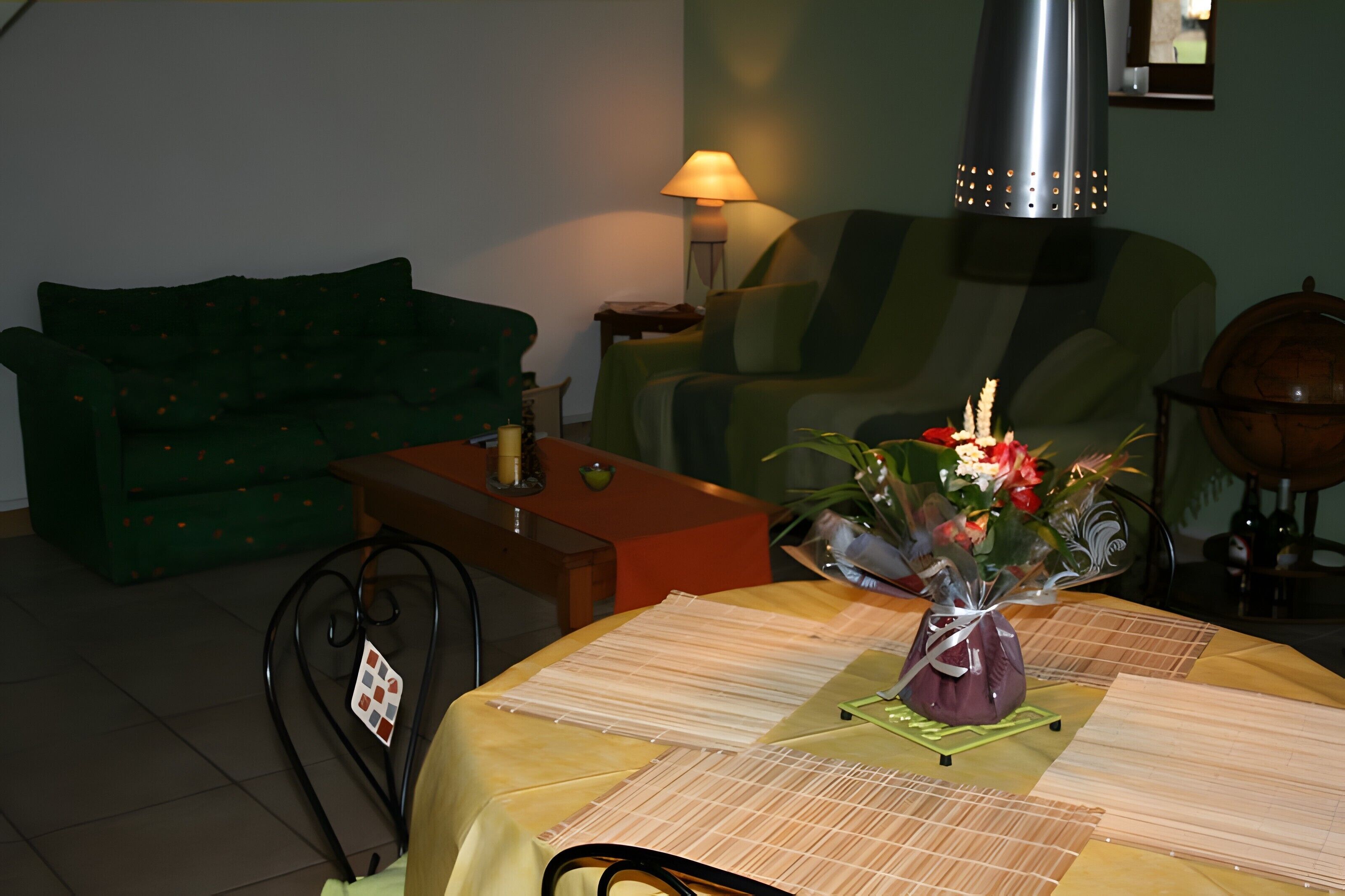 Un salon avec un canapé vert, une table basse en bois, une table à manger avec un set de table, une lampe et un globe terrestre.