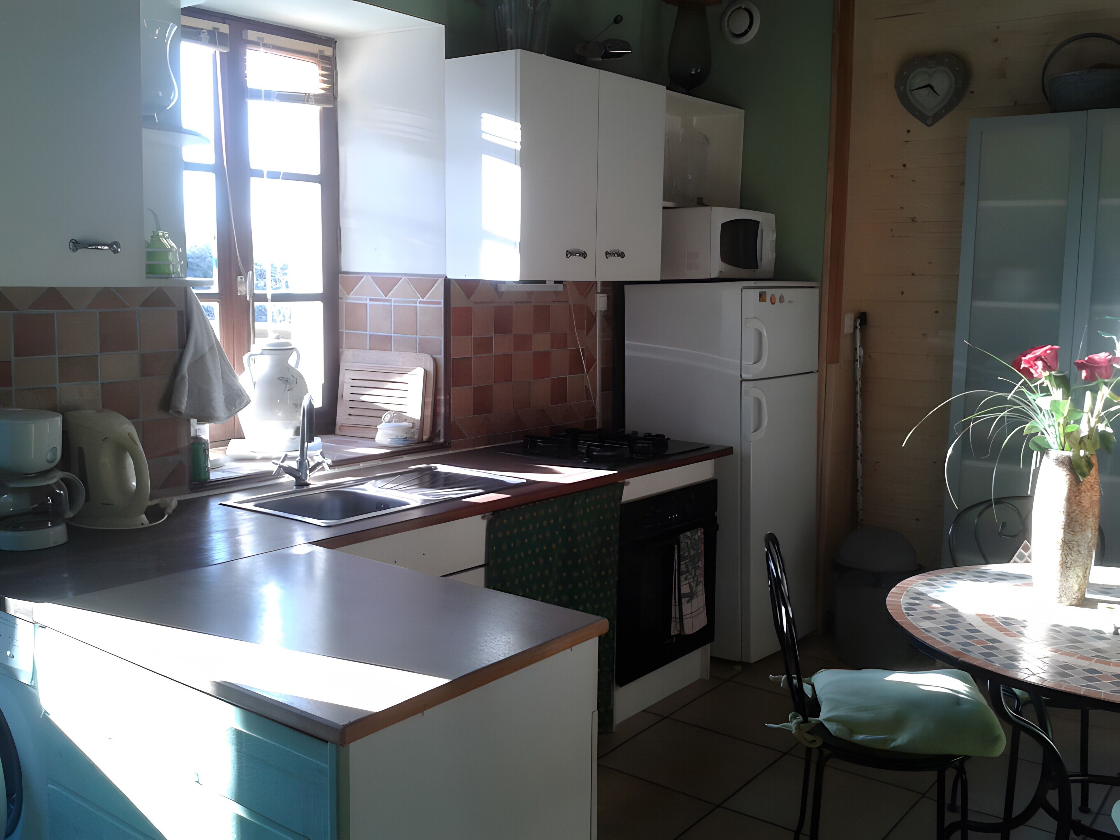 A kitchen with a sink, stove, and cabinets, a dining table with chairs, and a clock on the wall.