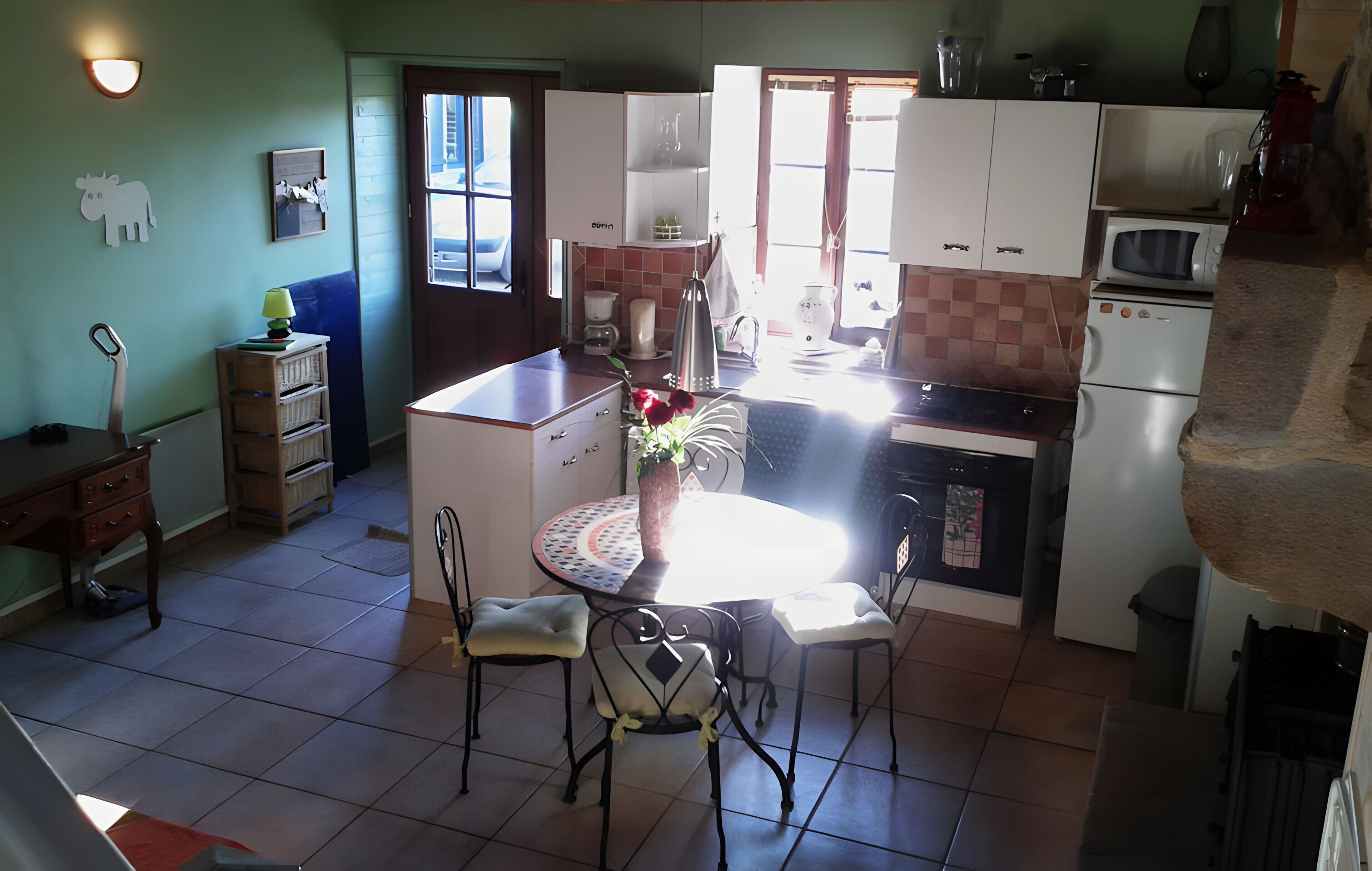 Une cuisine compacte avec des meubles blancs, une table à manger avec des chaises, un petit réfrigérateur et un four à micro-ondes.