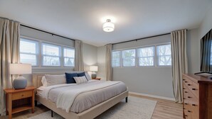A bedroom with a large bed, two bedside tables, a dresser, and a ceiling light. - Remodeled Home w/ Garage, Workspace & Fenced Yard (Racine)