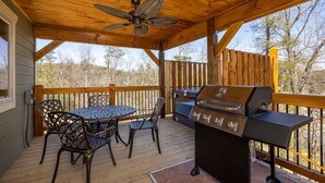 An outdoor deck with a wooden ceiling, a ceiling fan, a grill, and metal chairs. - Mountain High (Gatlinburg)