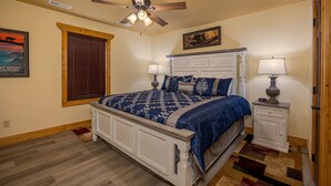 A bedroom with a bed, two bedside tables, a ceiling fan, a window with blinds, a wall-mounted picture, and a patterned rug. - Mountain High (Gatlinburg)