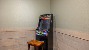 A single arcade machine with a colorful front panel, a small wooden stool, and a plain wall with horizontal wooden panels. - Mountain High (Gatlinburg)