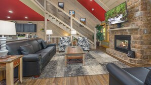 A spacious living room with a fireplace, a staircase, and a large TV mounted on a stone wall. - Smoky Mountain Plunge (Gatlinburg)