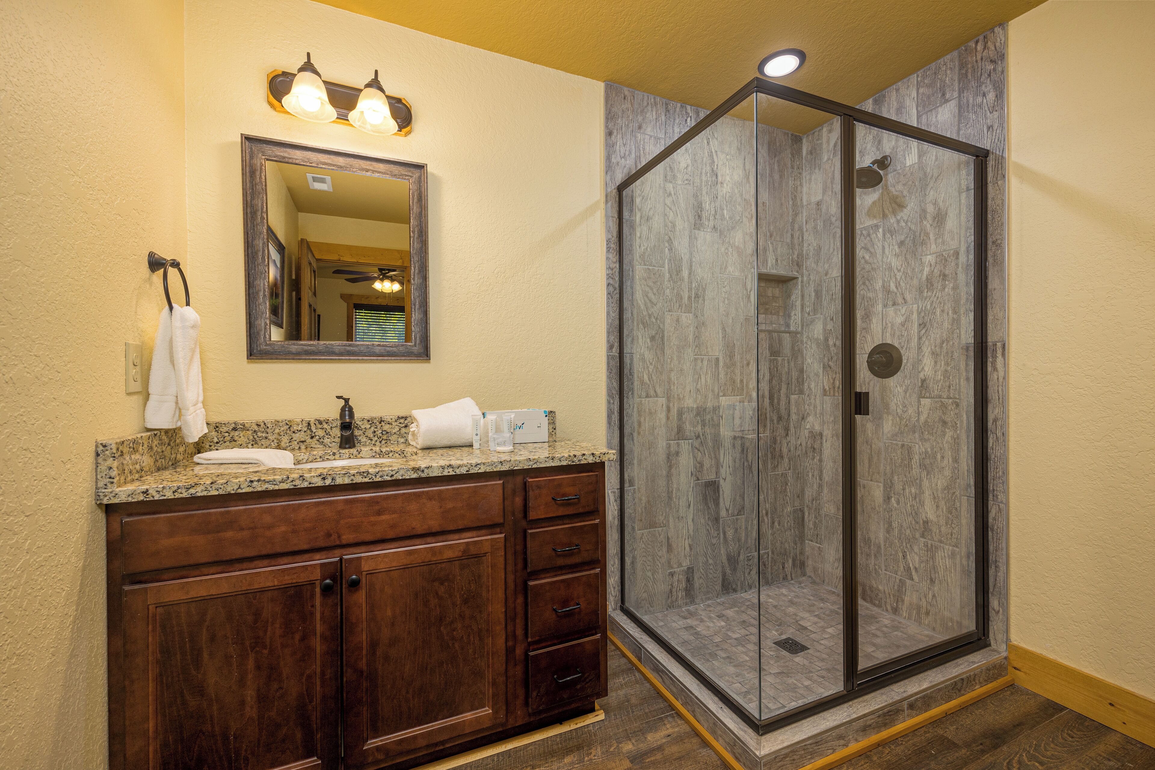 A bathroom with a wooden vanity, a mirror, and a glass-enclosed shower.