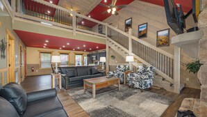 A spacious living area with a high ceiling, a staircase, and a view of the kitchen. - Smoky Mountain Plunge (Gatlinburg)