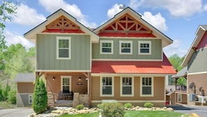 A two-story house with a stone foundation, a front porch with a bench, and a red roof. - Splash Mountain Lodge (Gatlinburg)