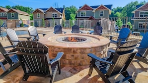 A patio area with Adirondack chairs, a stone fire pit, and a view of houses in the background. - Splash Mountain Lodge (Gatlinburg)