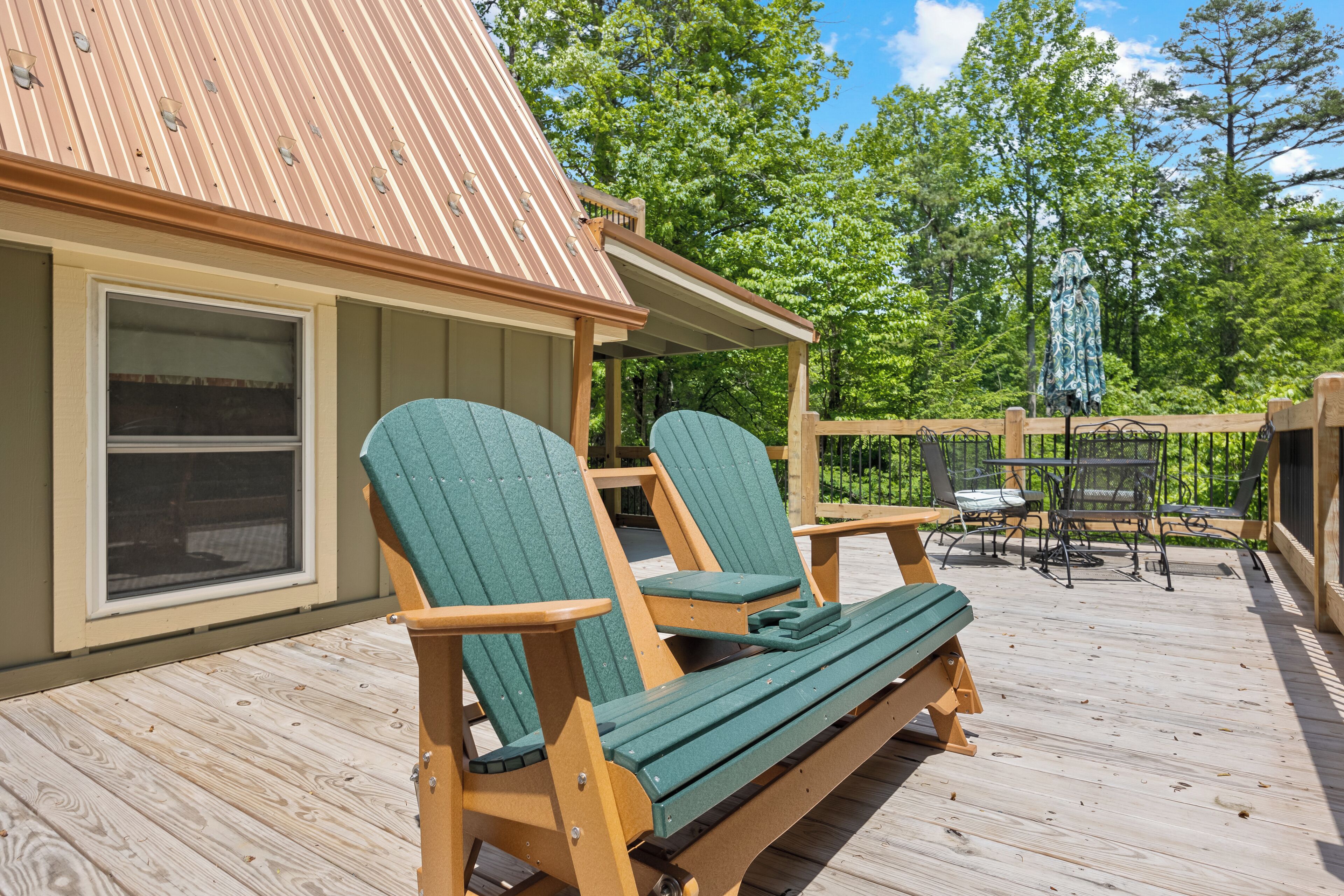 A wooden deck with two Adirondack chairs and a wooden table.