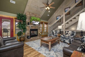 A spacious living room with a stone fireplace, wooden ceiling, and a large TV. - Harmony Peak (Gatlinburg)