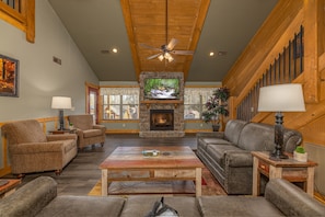 A cozy living room with a stone fireplace, comfortable seating, and a ceiling fan. - Chateaux Bliss (Gatlinburg)