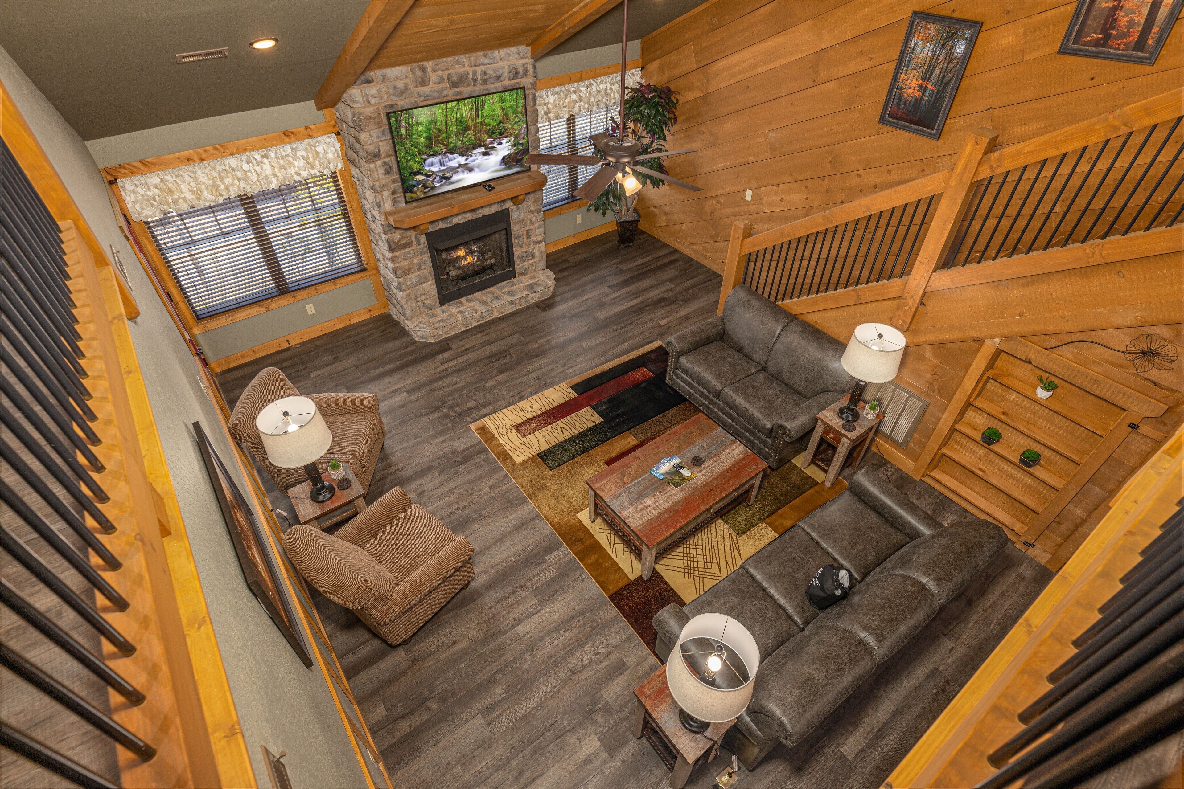 A spacious living area with a stone fireplace, wooden ceiling beams, and a large window overlooking a forest.