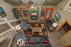 A spacious living area with a stone fireplace, a ceiling fan, and a large window with curtains. - Wet and Wild (Gatlinburg)