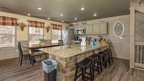 A kitchen with granite countertops, a central island with bar stools, a refrigerator, a microwave, and wooden cabinets. - Wet and Wild (Gatlinburg)