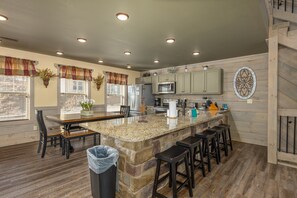 A kitchen with granite countertops, a central island with bar stools, a refrigerator, a microwave, and wooden cabinets. - Wet and Wild (Gatlinburg)