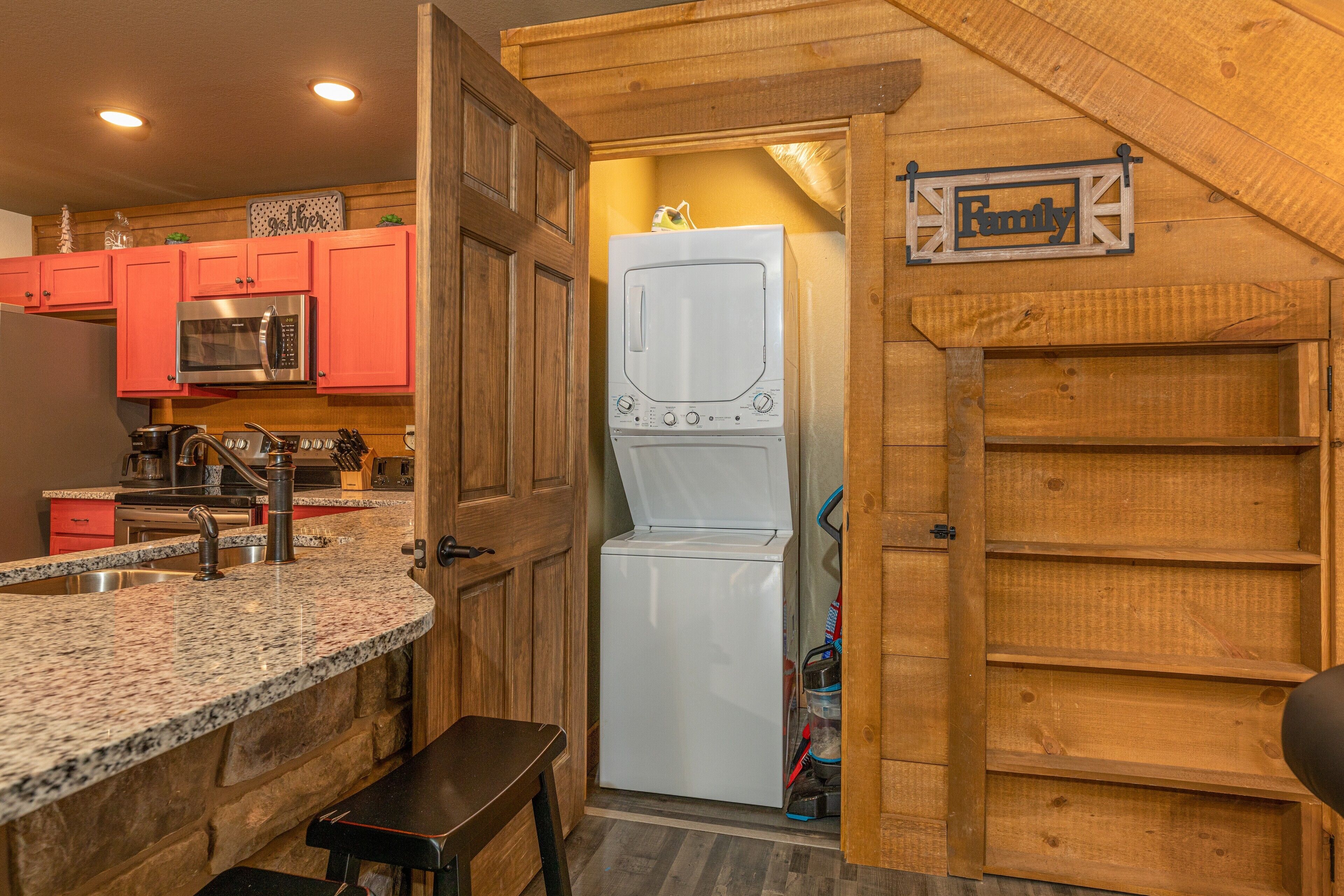 A compact kitchen with red cabinets, a granite countertop, a stainless steel microwave, and a white washing machine.