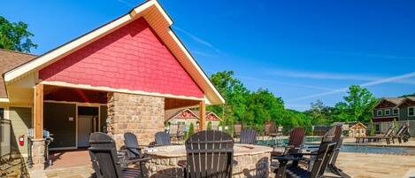 A covered outdoor seating area with Adirondack chairs and a fire pit, surrounded by a wooden deck and a stone wall.