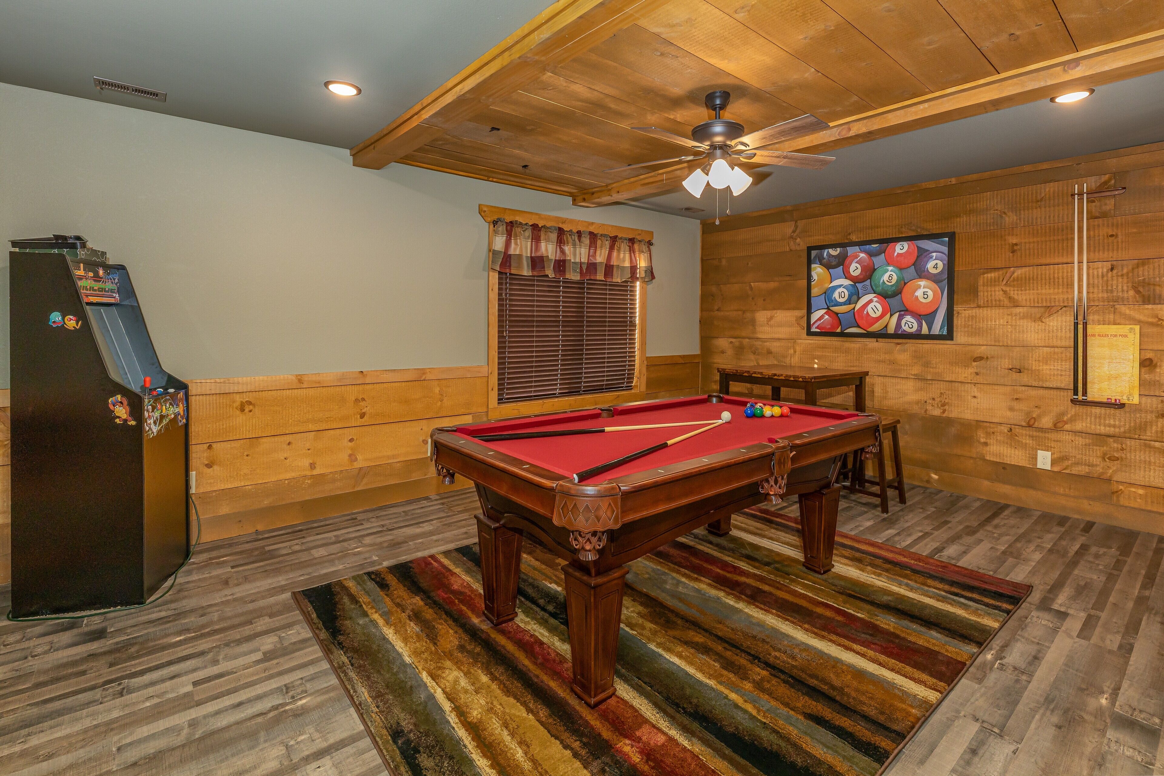 A pool table with a striped rug, a ceiling fan, and wooden walls.