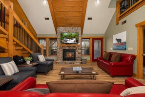 A spacious living room with a stone fireplace, a television mounted above it, and a red leather sofa. - Luna Bear Lodge (Gatlinburg)