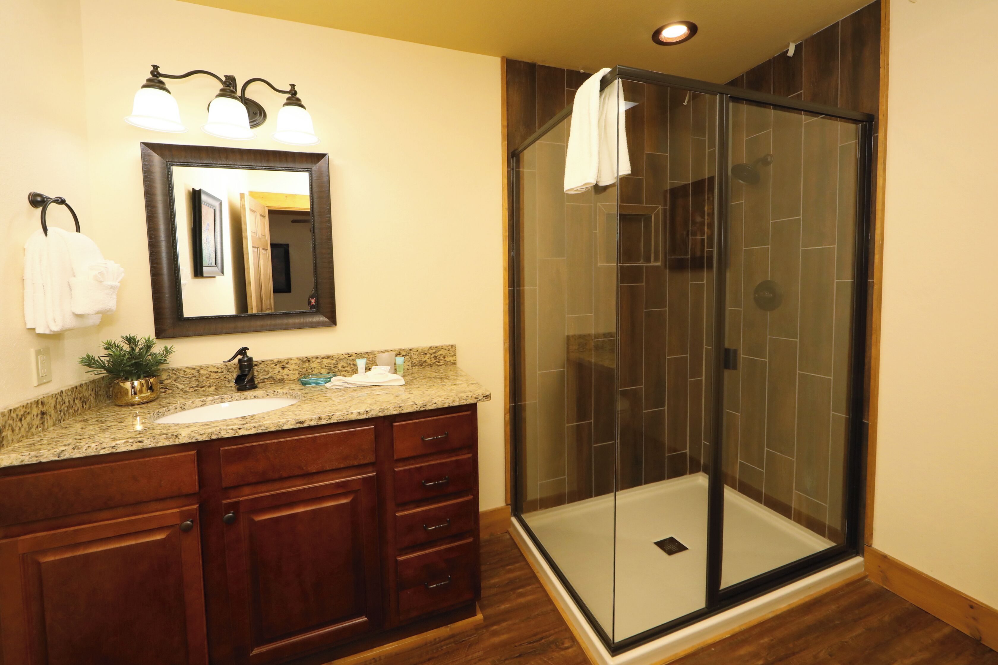 A bathroom with a granite countertop, a sink, a mirror, and a glass-enclosed shower area.