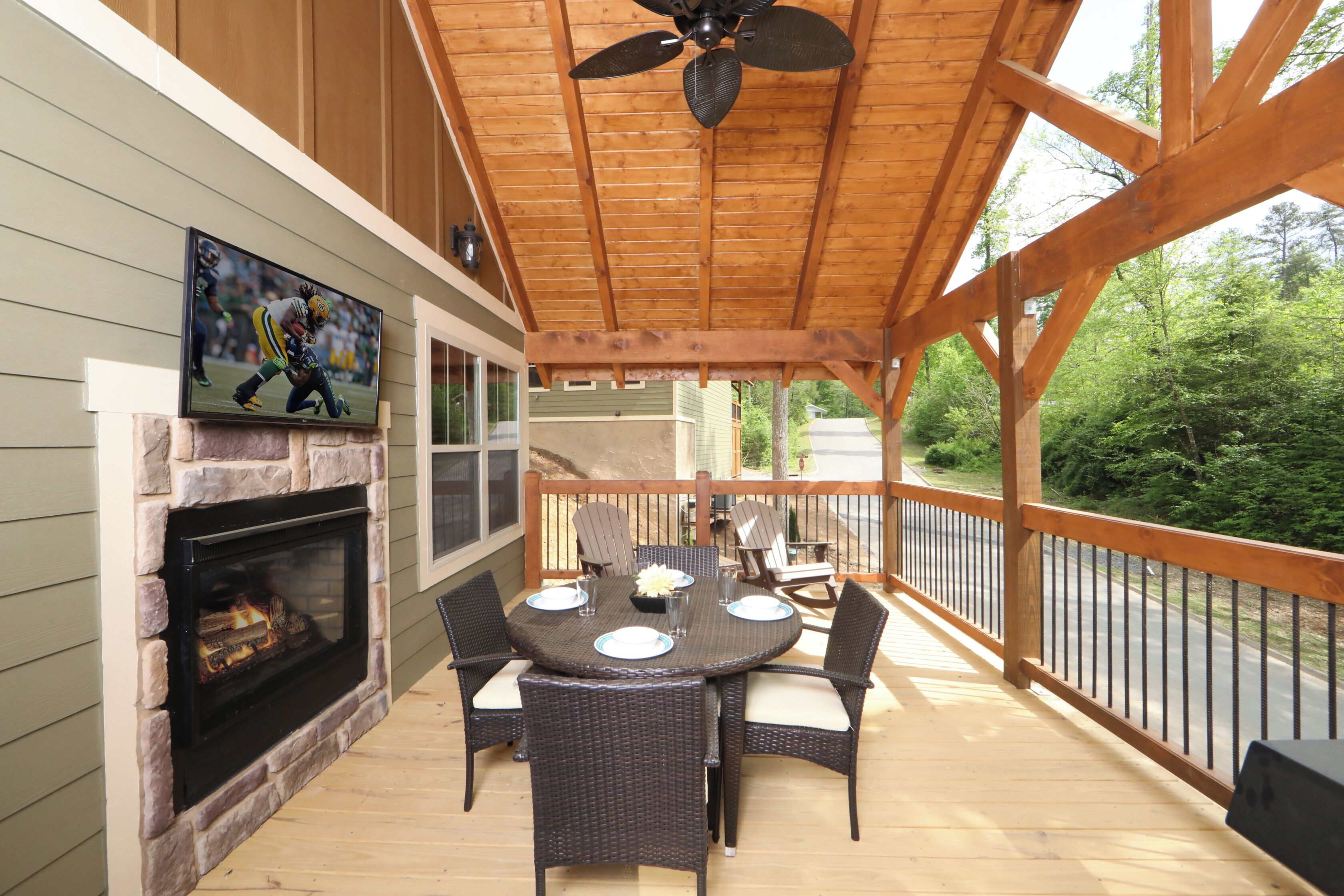 A covered outdoor patio with a round table, chairs, a fireplace, and a television mounted on the wall.