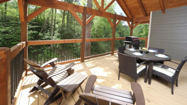 A wooden deck with a dining table and chairs, surrounded by a forest. - Head Over Hills (Gatlinburg)