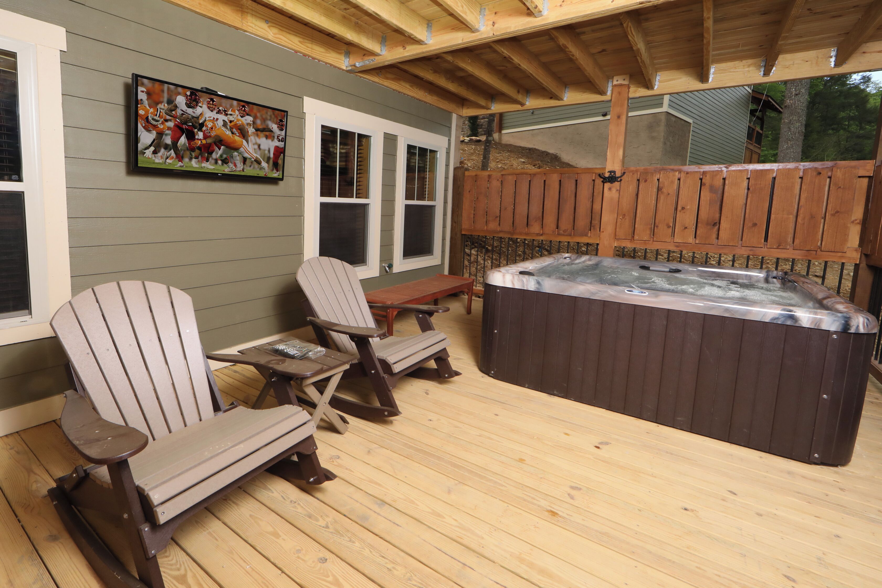 A covered patio with Adirondack chairs, a hot tub, and a TV mounted on the wall.
