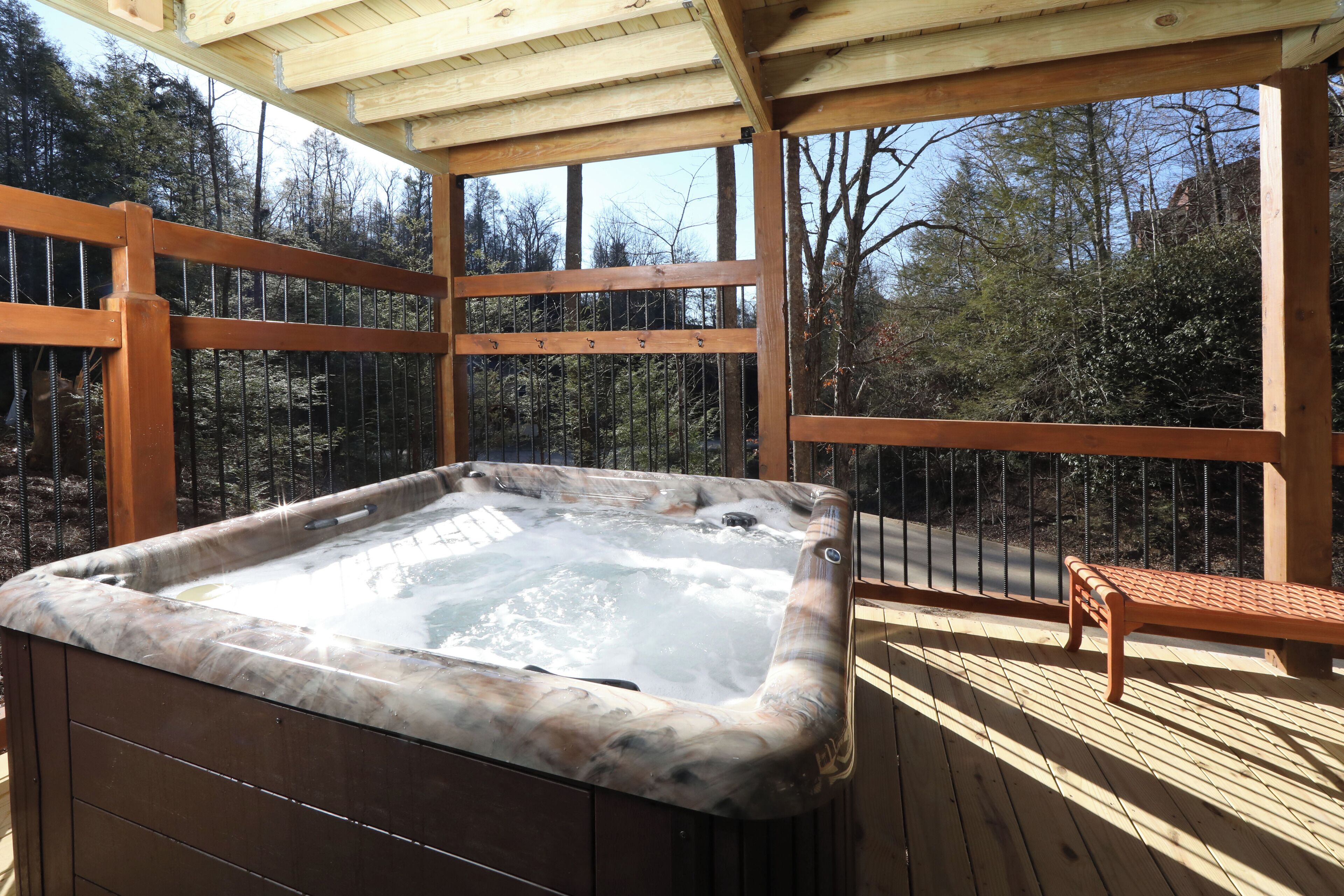 A hot tub on a wooden deck with a wooden railing and a bench.