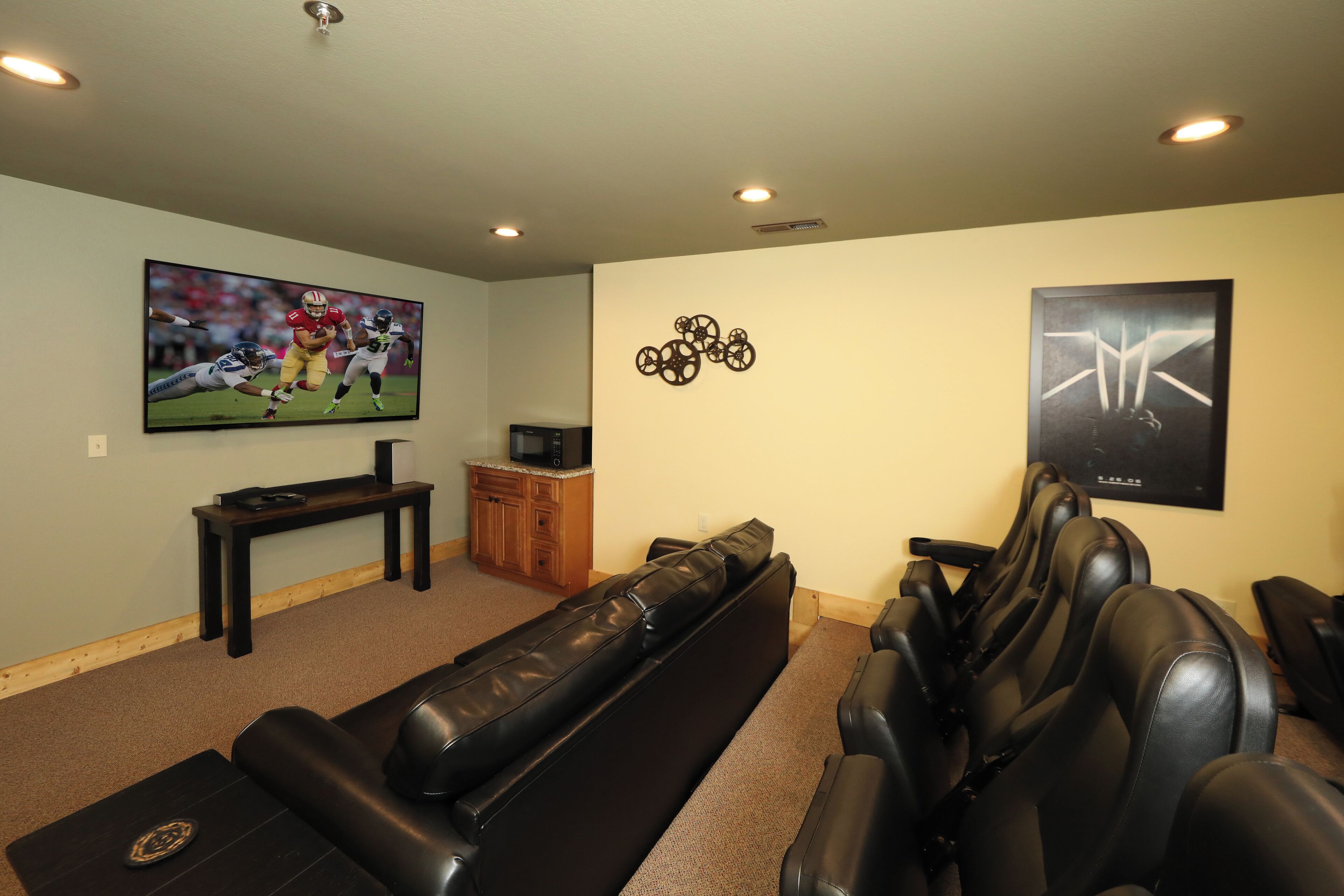 Un cine en casa con una televisión de pantalla grande, asientos de cuero negro y un mueble de madera.